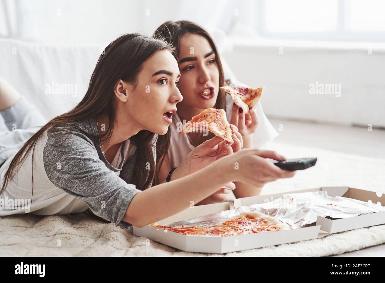Keine Möglichkeit, haben Sie gesehen. Schwestern essen Pizza beim Fernsehen, während auf dem Boden des schönen Schlafzimmer tagsüber liegen Stockfoto