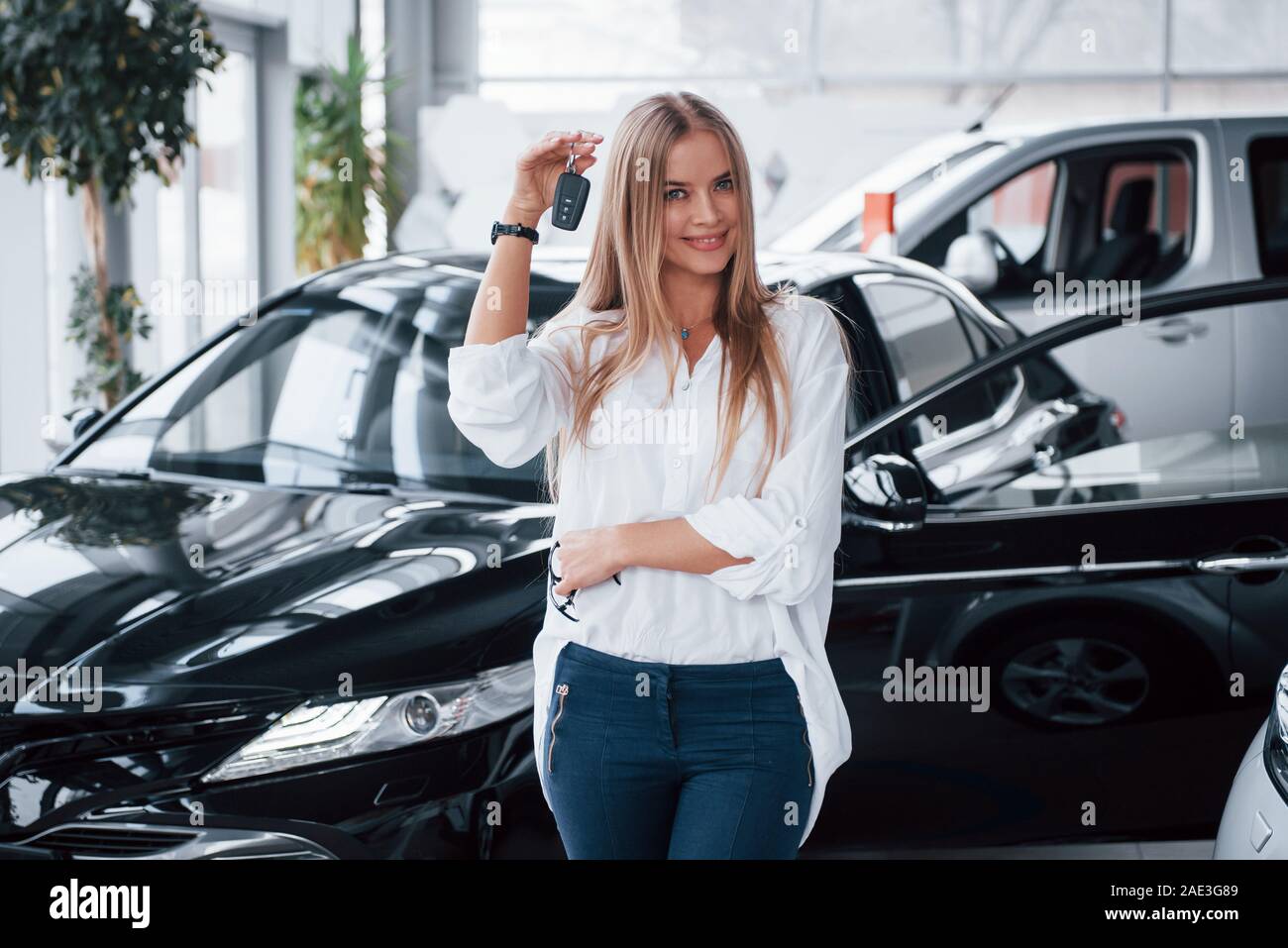 In Jeans und weißem T-Shirt. Junge Manager im Auto Shop steht gegen perfekt poliert schwarzes Auto Stockfoto