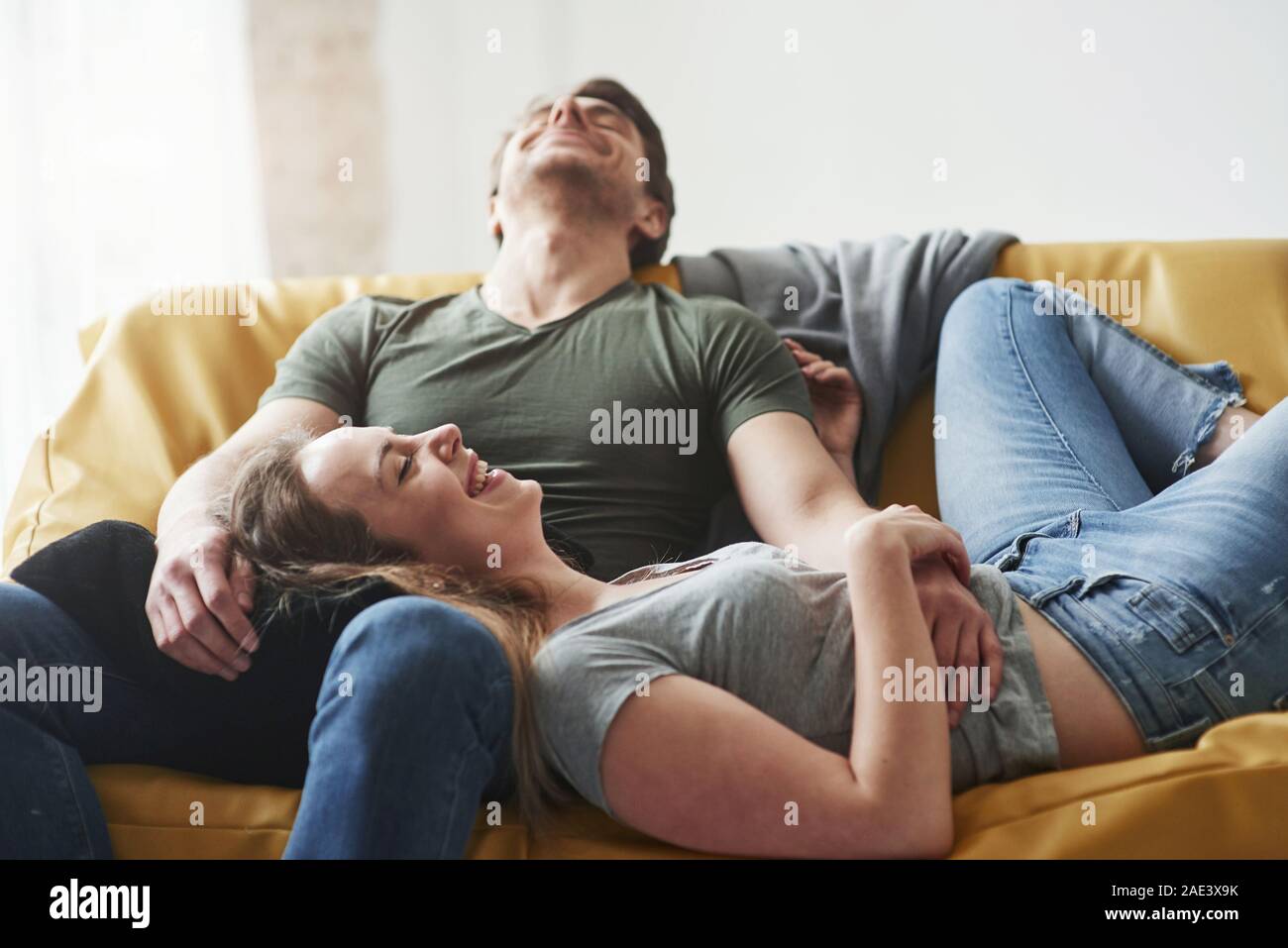 Netter Witz. Glückliches Paar entspannende auf dem gelben Sofa im Wohnzimmer ihres neuen Hauses Stockfoto