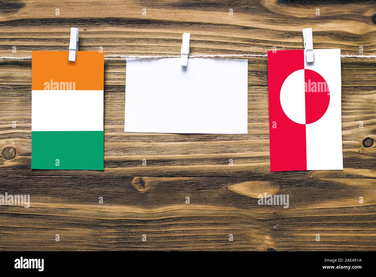 Hängenden Flaggen von Côte d'Ivoire und Grönland zu Seil mit wäscheklammer mit Kopie Raum befestigt auf weißem Papier auf Holz- Hintergrund. Diplomatischen re Stockfoto