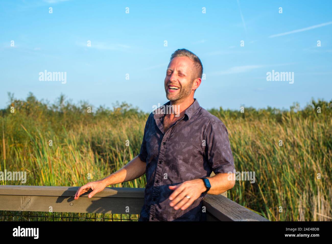 Ein glücklicher Mann lehnt sich an ein Geländer in einer Wetland Park lachen Stockfoto