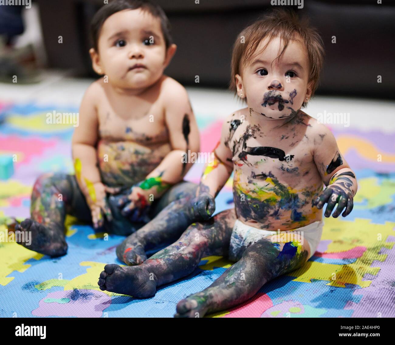 Baby Mädchen mit unordentlichen bemaltem Gesicht sitzen auf dem Boden Stockfoto