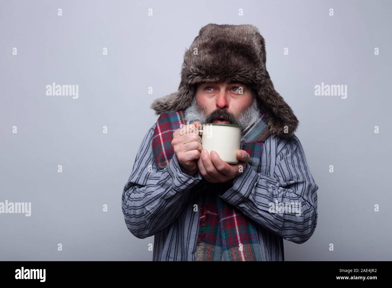 Menschen leiden an einer Grippe mit Schlafanzug und mit einer Kappe weht eine heiße Tasse Tee auf einem grauen Hintergrund zu warm. Gesundheit Konzept. Stockfoto
