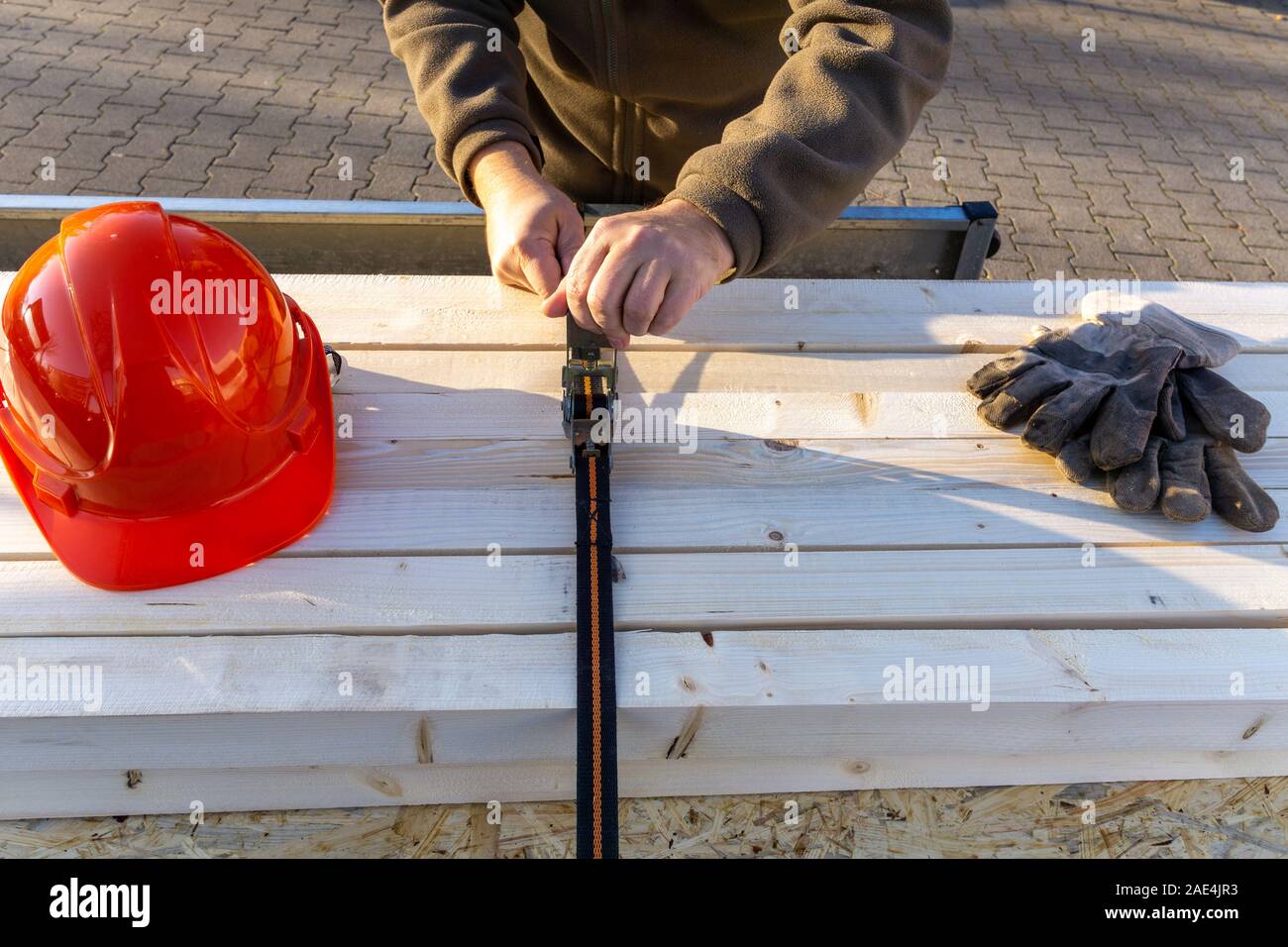 Bauarbeiter sichert Last auf einem PKW-Anhänger mit Spannbändern Stockfoto