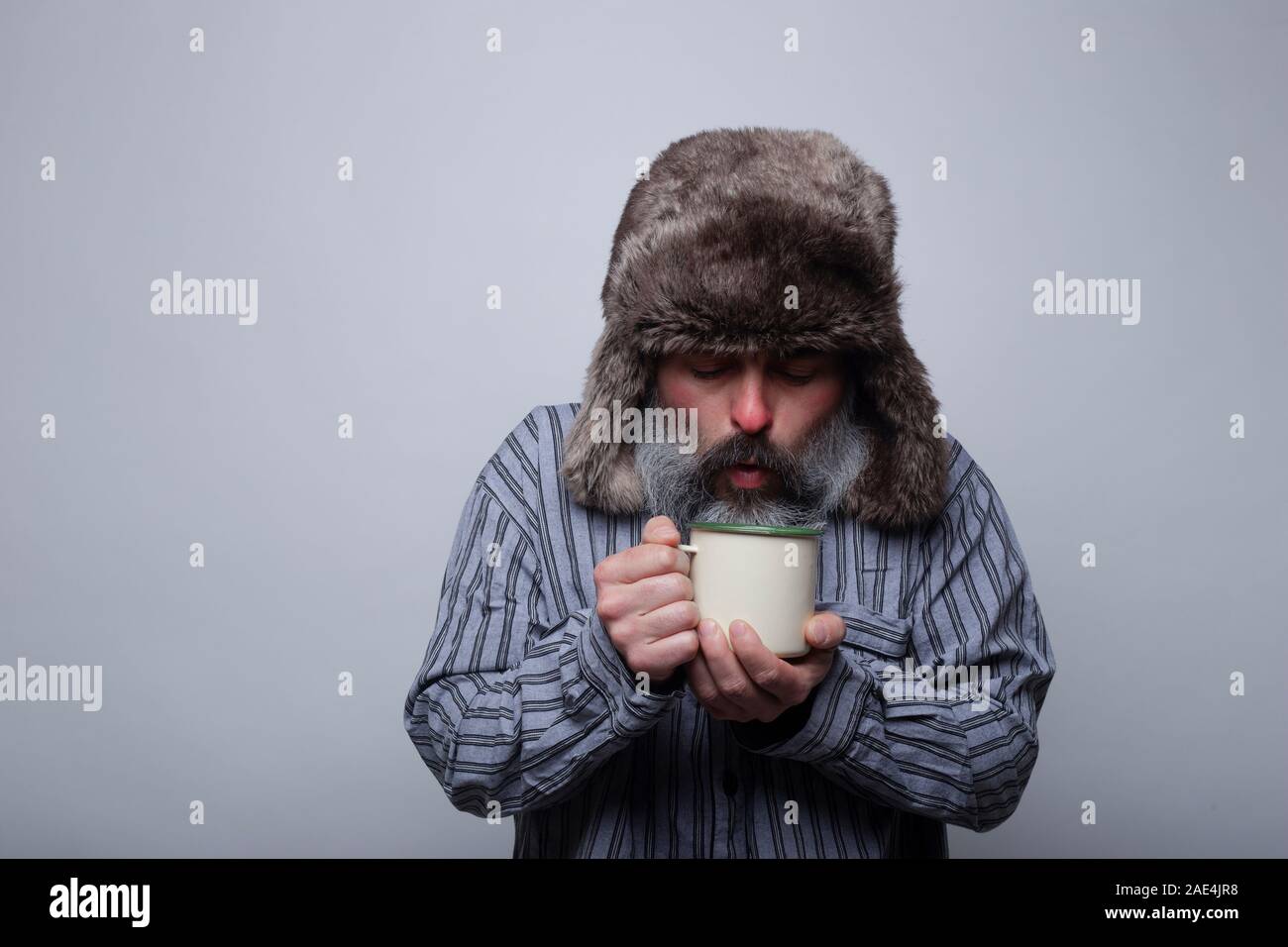 Grippe kranken Mann mit Schlafanzug und mit einer Kappe weht eine heiße  Tasse Tee auf einem grauen Hintergrund. Gesundheit Konzept Stockfotografie  - Alamy