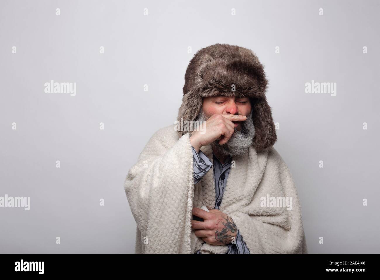 Fetter Mann mit Kappe und Decke über seine Nase beim Niesen. Auf grauem Hintergrund. Gesundheit Konzept.... Stockfoto