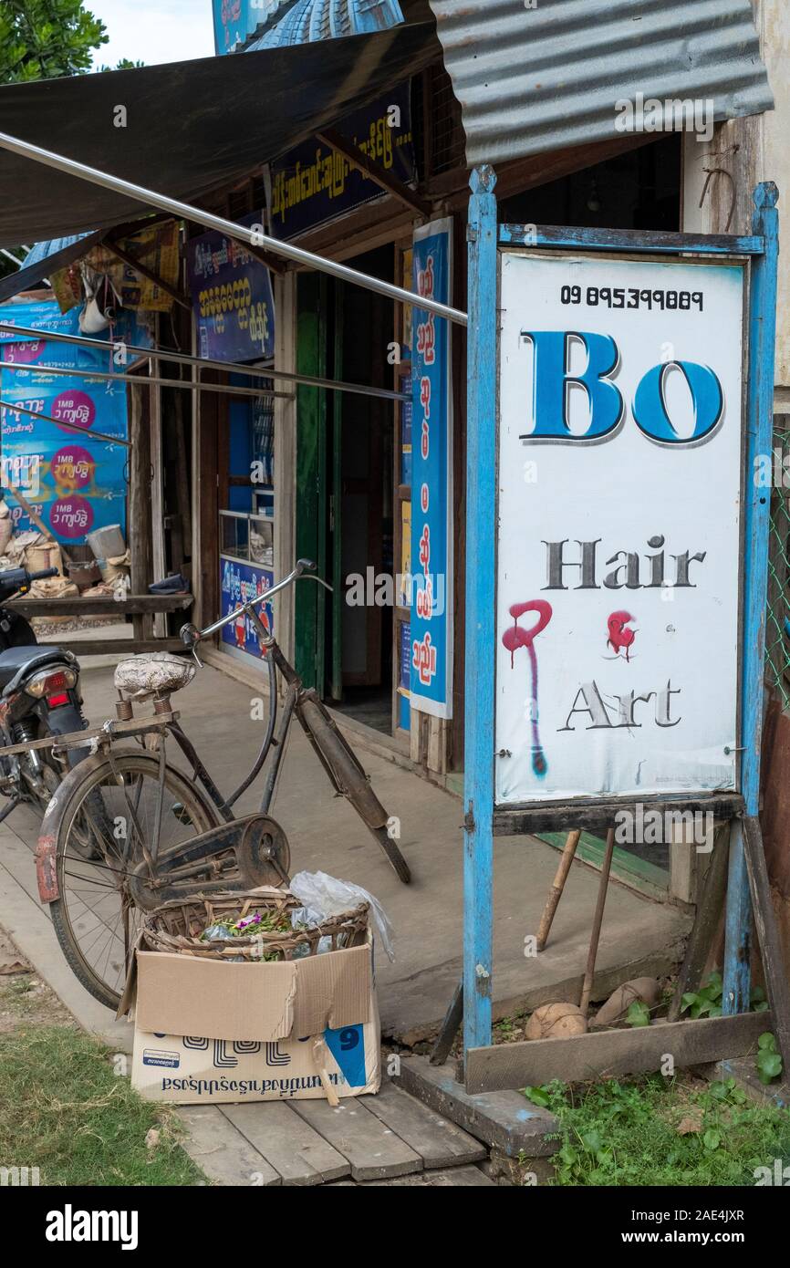 Einfache open-air Friseur mit Friseur- warten auf die Kunden während der Kontrolle sein Mobiltelefon in Homalin, nordwestliche Myanmar (Birma) Stockfoto