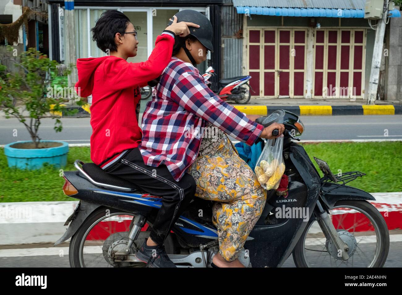 Burmesischen Mutter & Tochter auf einem Moped mit der Tochter drücken Helm der Mutter zu niedrig für Sie zu sehen, auf den Straßen von Mandalay, Myanmar (Birma) Stockfoto
