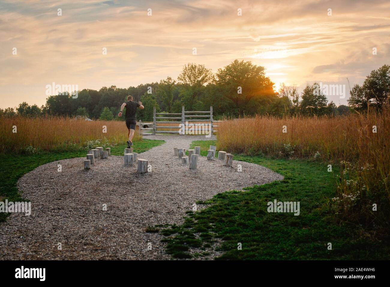 Ein Mann läuft über Serie von Holzbalken im Hindernislauf bei Sonnenuntergang Stockfoto