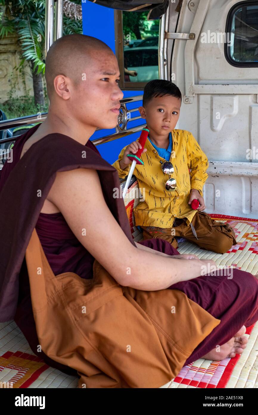 Ein junger buddhistischer Mönch und ein kleiner Junge mit einem Kunststoff Messer sitzen auf einer Matte in der Rückseite eines jitney Bus warten in Mandalay, Myanmar (Birma) Stockfoto