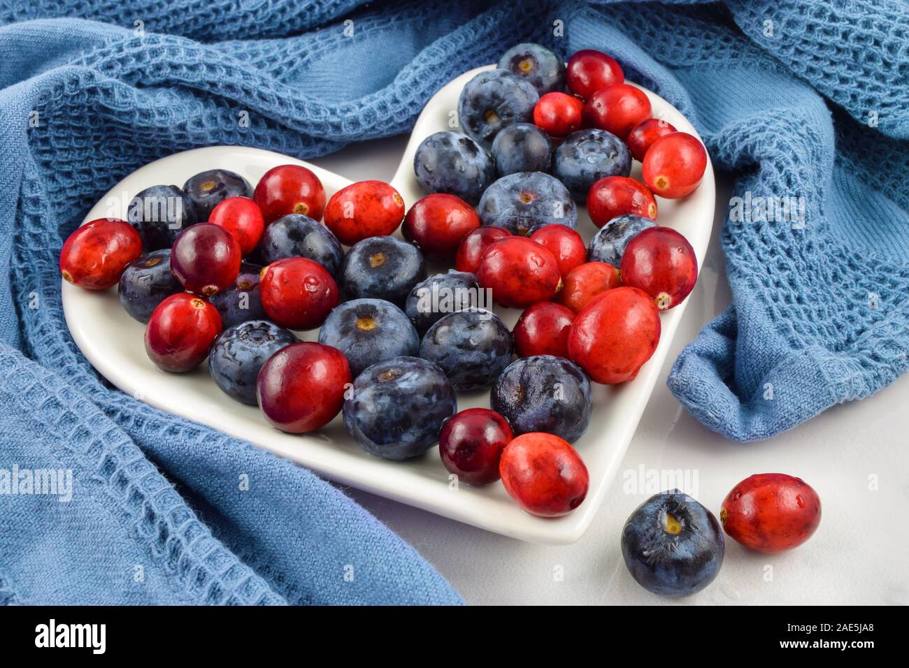 Das gesunde Herz Preiselbeeren und Blaubeeren schmücken eine herzförmige Platte durch ein blaues Handtuch für die Küche umgeben. Toll für Independence Day, Memorial Day und V Stockfoto