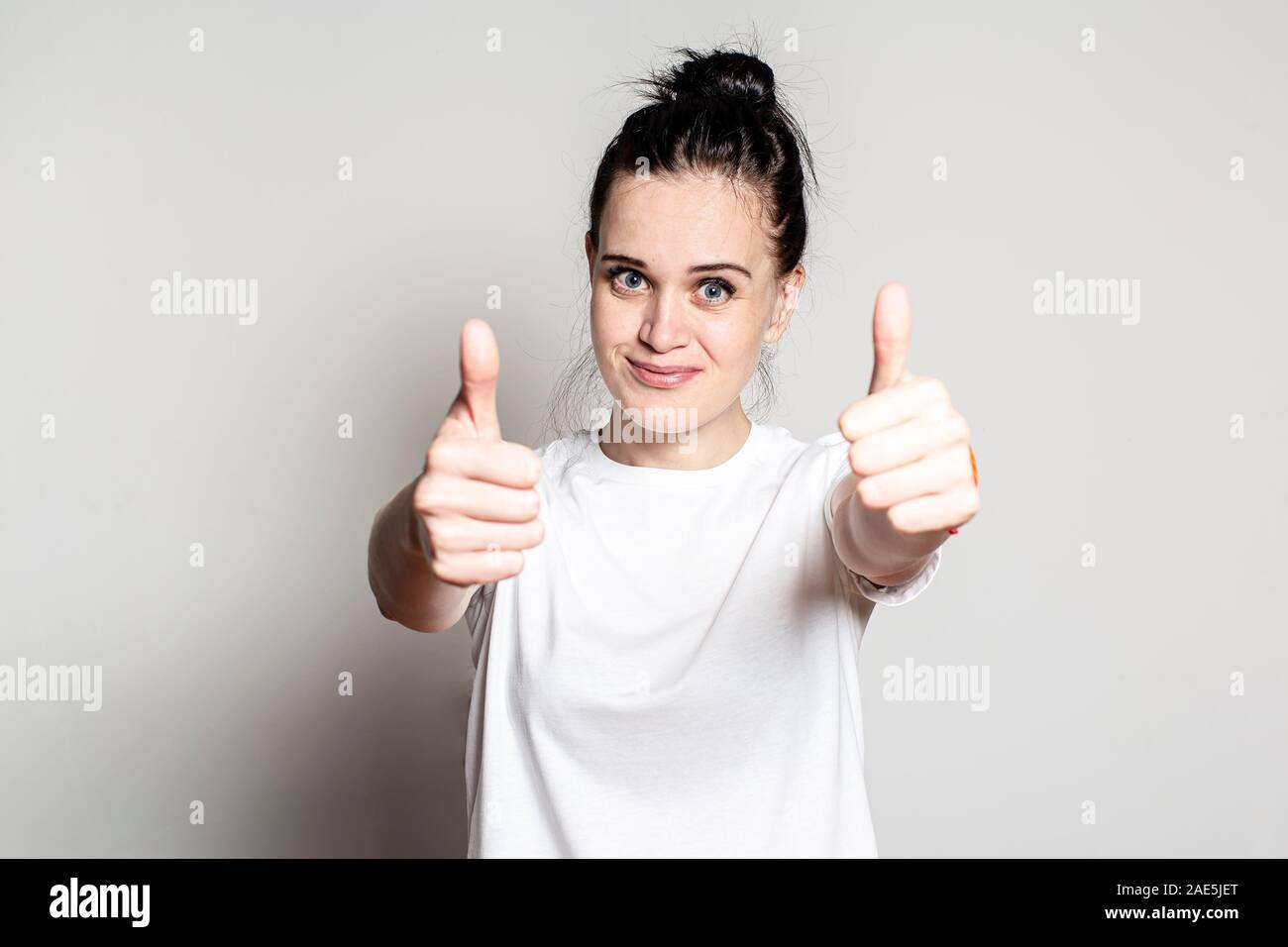 Positive junge Frau, eine grosse Hand Daumen oben-Geste, lächelnd und mit Blick auf die Kamera. Konzept der Genehmigung und Erfolg. Stockfoto