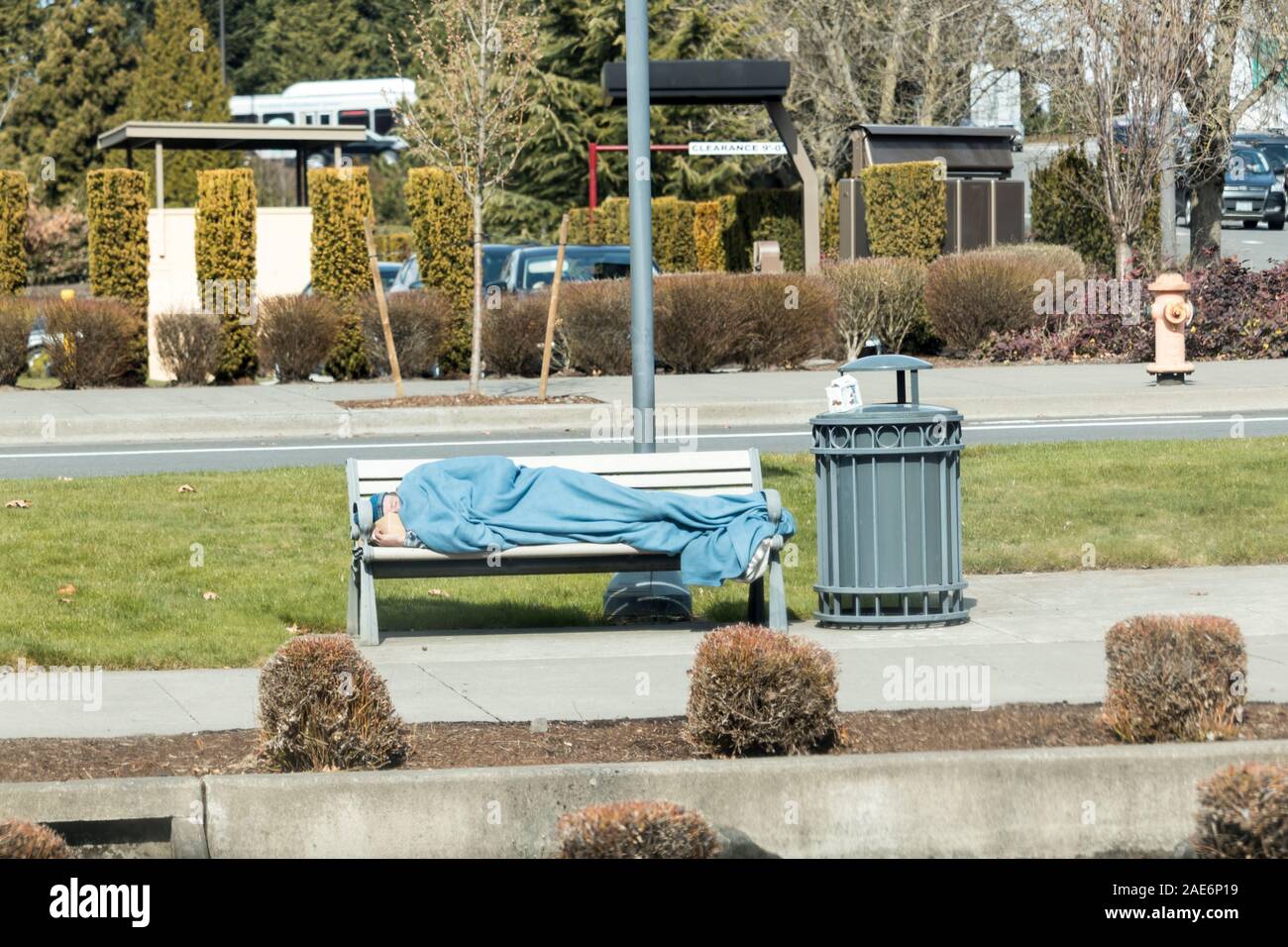 Portland, Oregon. Circa 2019. Obdachlosen mit einer Decke schlafen auf eine Bank fallen neben einer Mülltonne. Stockfoto