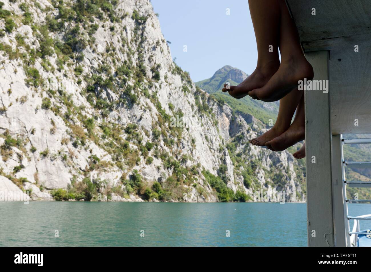 Nahaufnahme der Passagiere ihre Beine und Füße baumeln von der Reling und geniessen Sie die herrliche Landschaft auf der Komani See, Albanien Stockfoto