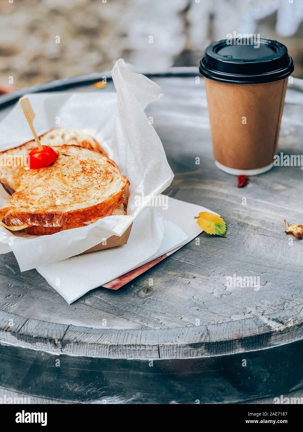 Panini mit Schinken und Käse sandwich Papier mit Kaffee Tasse auf einem hölzernen Tisch im Freien serviert. Street Market essen weg Konzept Stockfoto