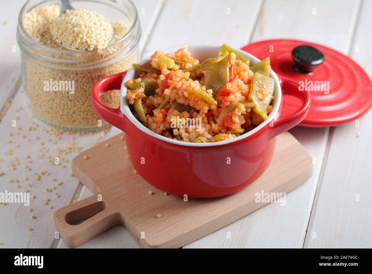 Millet Porridge mit grünen Bohnen und Tomaten in rot Teller auf einem rustikalen Tisch Stockfoto