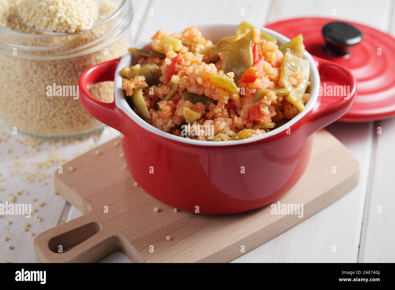 Millet Porridge mit grünen Bohnen und Tomaten in rot Teller auf einem rustikalen Tisch Stockfoto