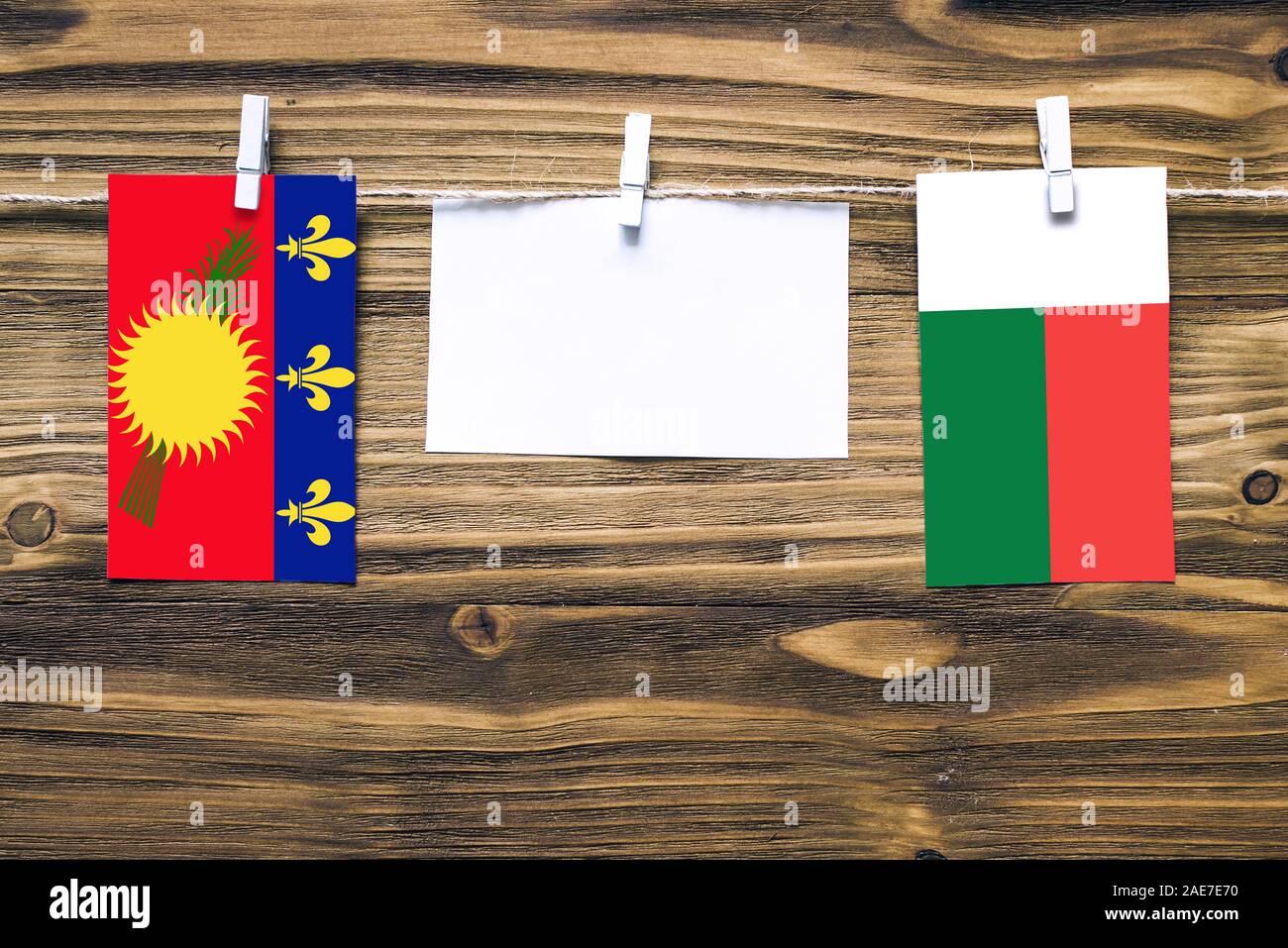 Hängenden Flaggen von Guadeloupe und Madagaskar zu Seil mit wäscheklammer mit Kopie Raum befestigt auf weißem Papier auf Holz- Hintergrund. Diplomatische Beziehungen Stockfoto