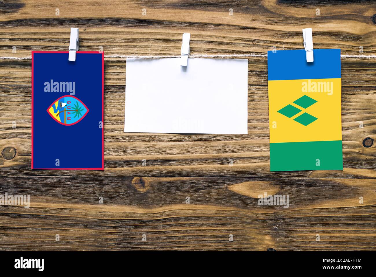 Hängenden Flaggen von Guam und St. Vincent und den Grenadinen zum Seil mit Kleidung Pins mit Kopie Raum befestigt auf weißem Papier auf Holz- Hintergrund Stockfoto