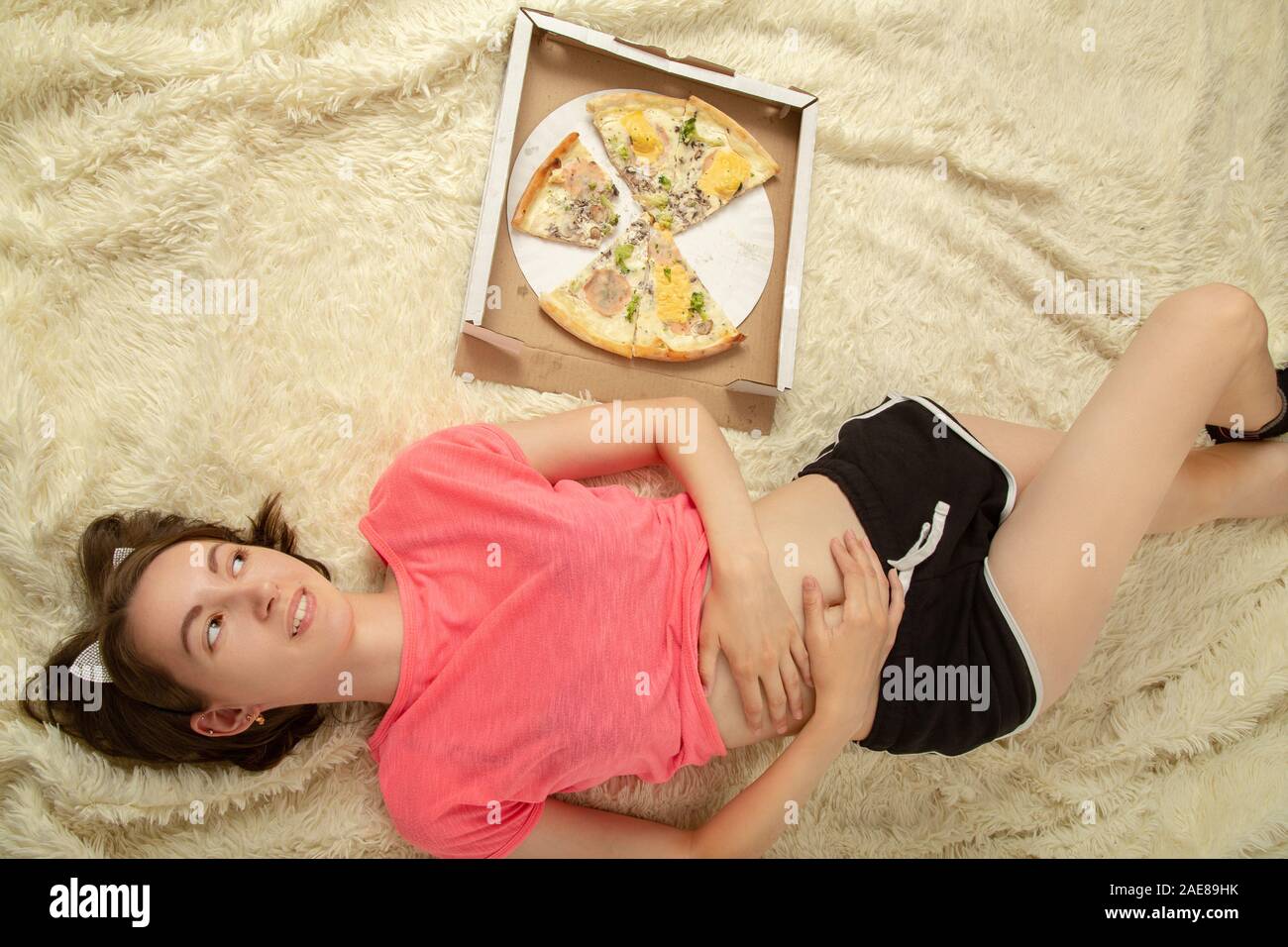 Spaß glücklich Überessen Mädchen liegt mit Pizza Stücke Stockfoto