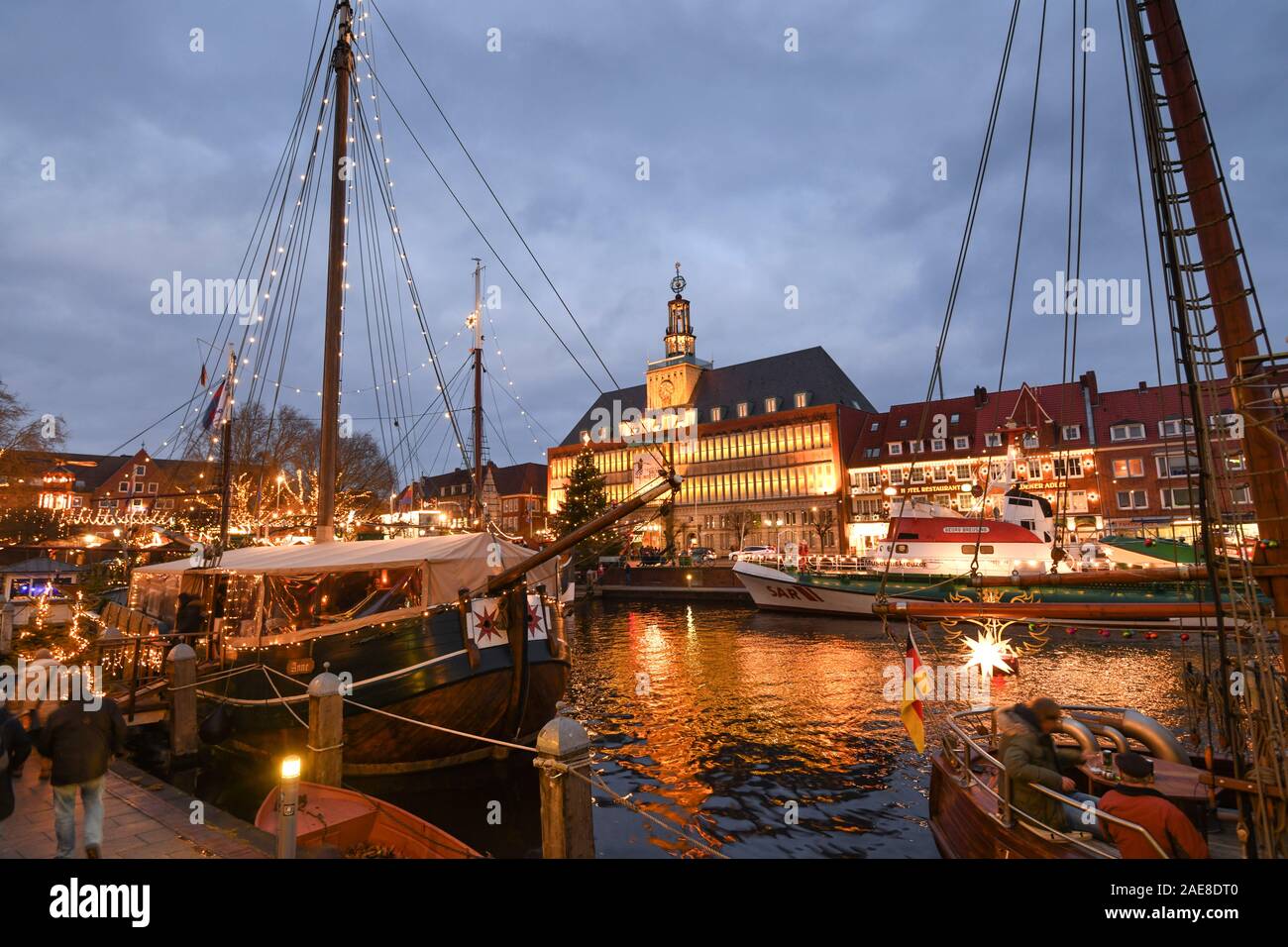 Emden, Deutschland. 07 Dez, 2019. Weihnachtliche Atmosphäre an der Emder Engelkemarkt. Besucher auf dem Weihnachtsmarkt schlendern Sie durch die festlich beleuchtete Schiffe entlang der Ratsdelft. Im Hintergrund das festlich beleuchtete Emder Rathaus. Credit: Karsten Klama/dpa/Alamy leben Nachrichten Stockfoto