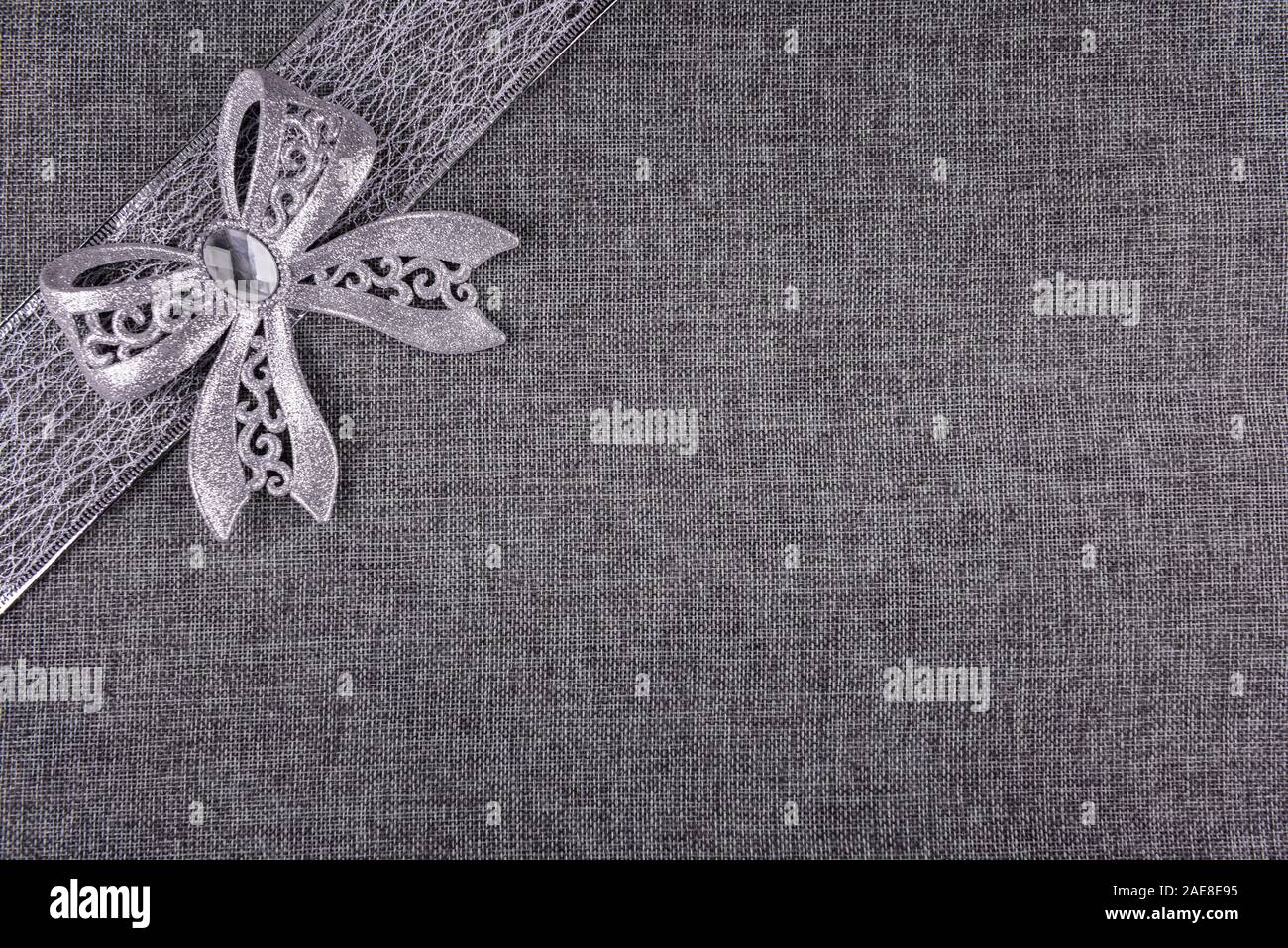 Elegante glänzende gebunden Silber glitter Bug auf Silber Farbband und auf Grau sackleinen. Horizontale Grußkarte Hintergrund mit großen Raum ein Kopieren Stockfoto