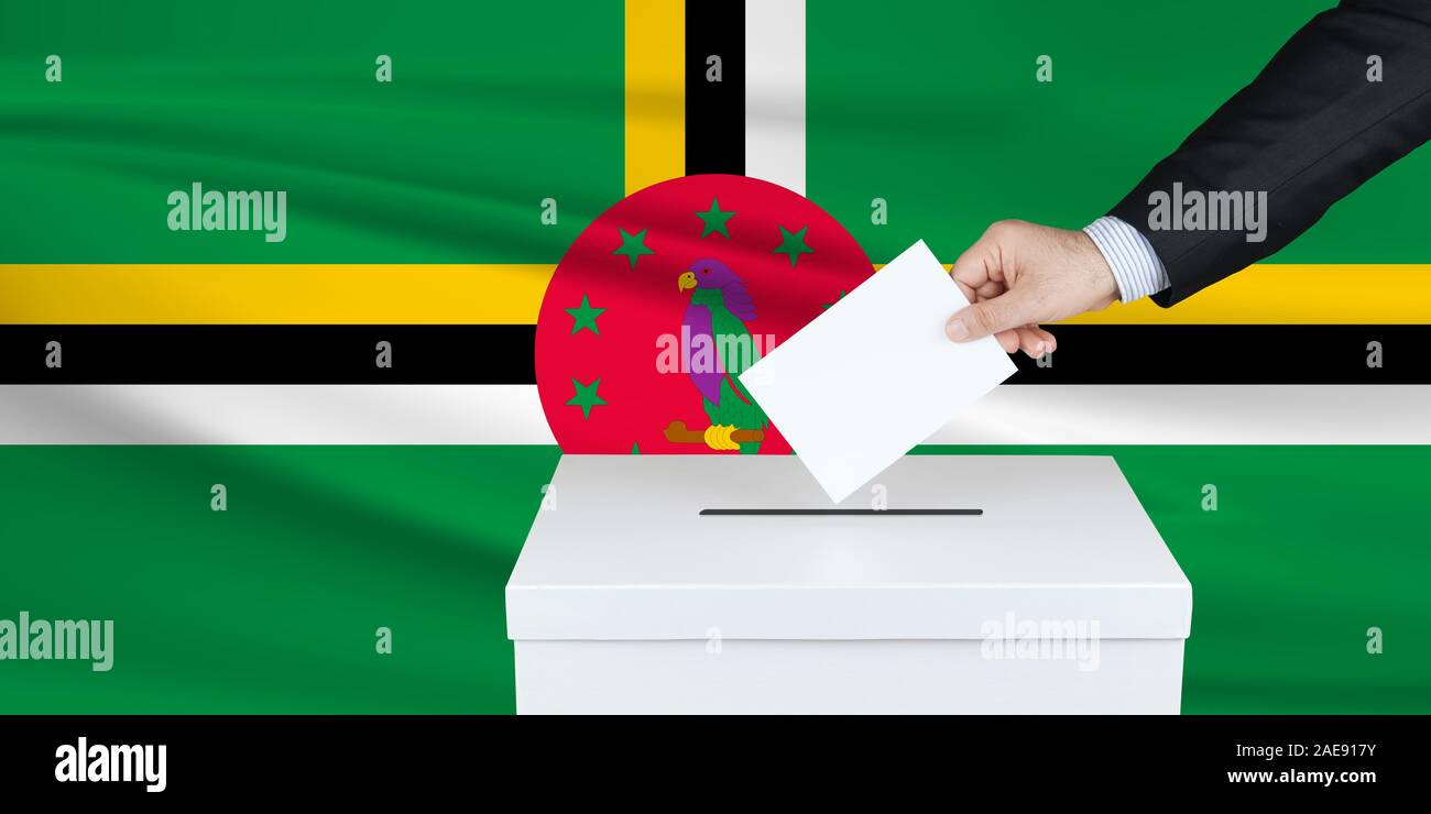 Wahl in Domenica. Die Hand des Menschen, der seine Stimme in die Wahlurne setzt. Winkte Domenica-Flagge auf Hintergrund. Stockfoto