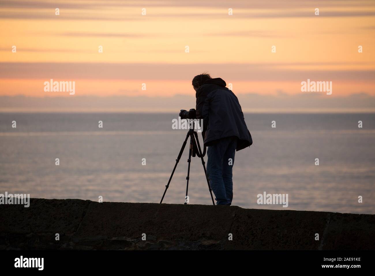 Ein Fotograf in der Dämmerung an einem frostigen Morgen Anfang Dezember stehen auf dem Cobb fotografieren den Sonnenaufgang und die Küste. Lyme Regis ist si Stockfoto