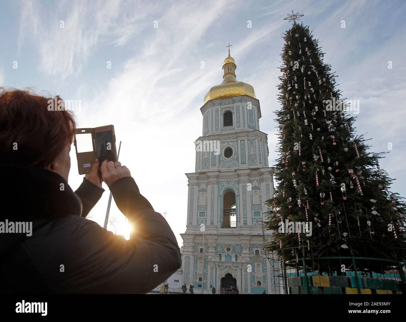 Eine Frau nimmt ein Foto der wichtigsten Weihnachtsbaum auf St. Sophia in Kiew. Die wichtigsten Weihnachtsbaum des Landes, deren Höhe mehr als 20 Meter hoch, wird mit 800 themed Spielwaren und mehr als 3 km von bunten Girlanden dekoriert, entsprechend dem offiziellen Portal der ukrainischen Hauptstadt. Riesige Figuren der Nussknacker und Helden der animierten Serie über Kosaken wird 'bewacht' durch den Weihnachtsbaum. Die wichtigsten ukrainischen Weihnachtsbaum auf St. Sophia in Kiew ist eine der schönsten Weihnachtsbäume in Europa im Jahr 2019, nach der besten europäischen Destinationen, wie Ukrainische Stockfoto