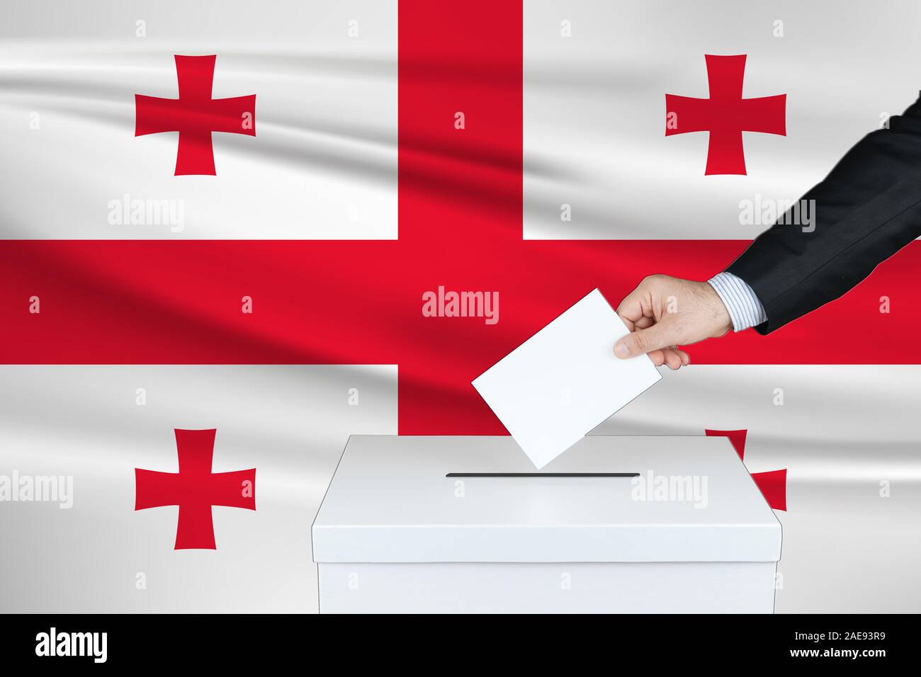 Wahl in Georgien. Die Hand des Menschen, der seine Stimme in die Wahlurne setzt. Gewinkte Flagge Georgiens auf Hintergrund. Stockfoto