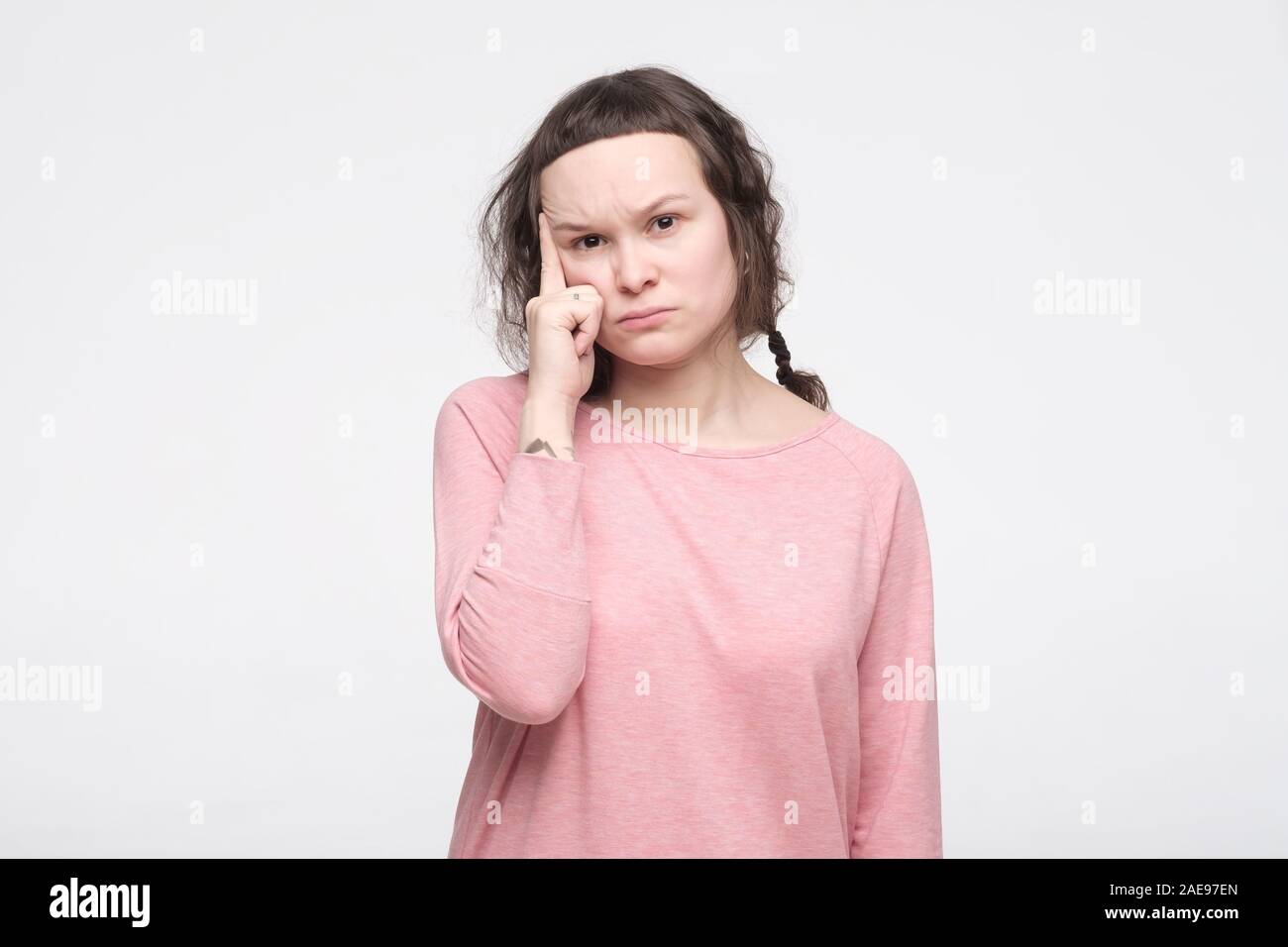 Nachdenklich konzentriert junge Frau in rosa Kleidung mit attraktiven Look versucht, etwas daran zu erinnern. Studio shot Stockfoto