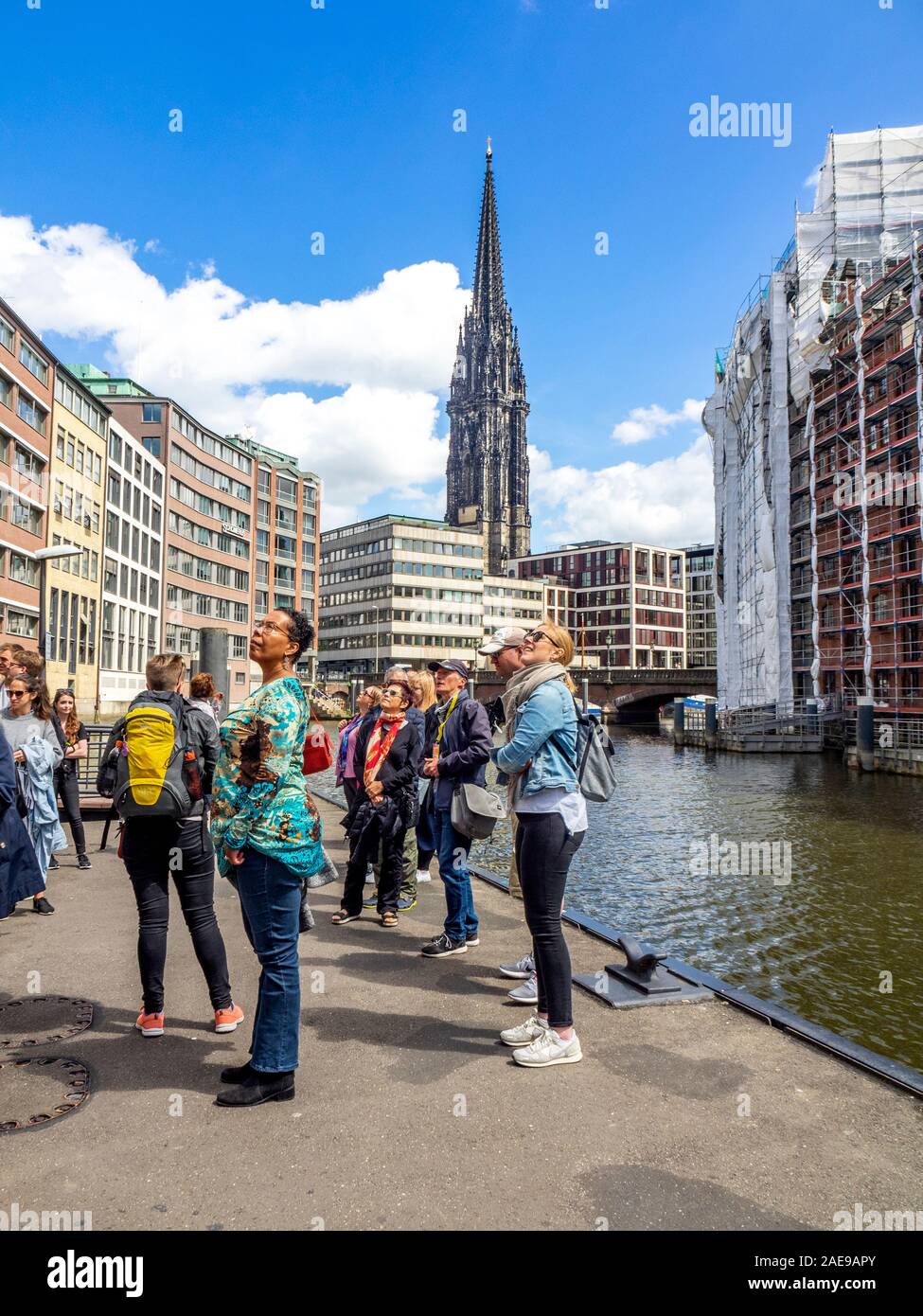 Geführte Wanderung Gruppentouristen auf einem Gehweg am Nikolaifleet-Kanal mit Blick auf historische Gebäude und die Gotische St. Nikolauskirche Hamburg Deutschland Stockfoto
