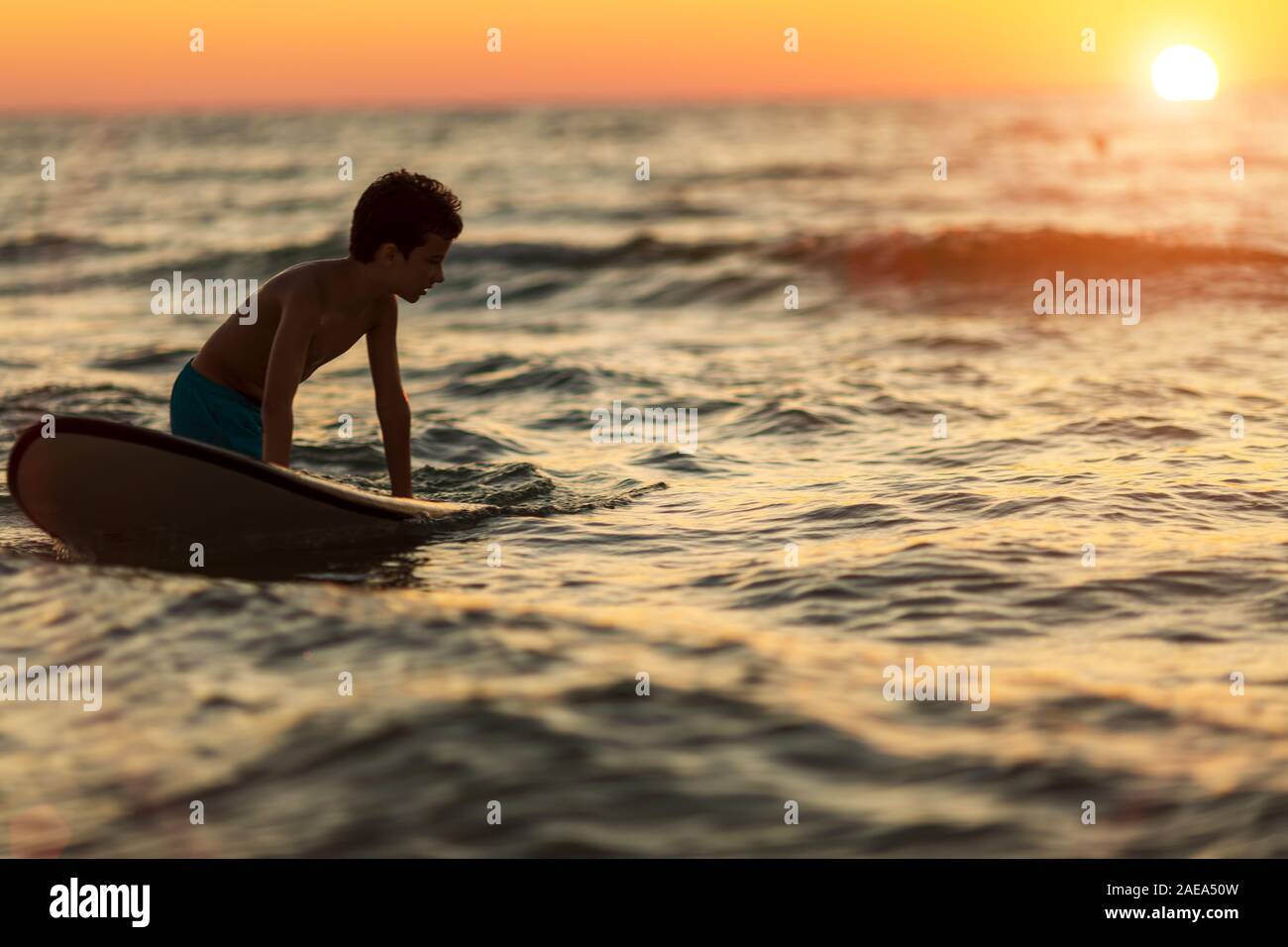 Silhouette eines Kindes mit einem Surfbrett in der DEFOKUSSIEREN in den Abendstunden Stockfoto