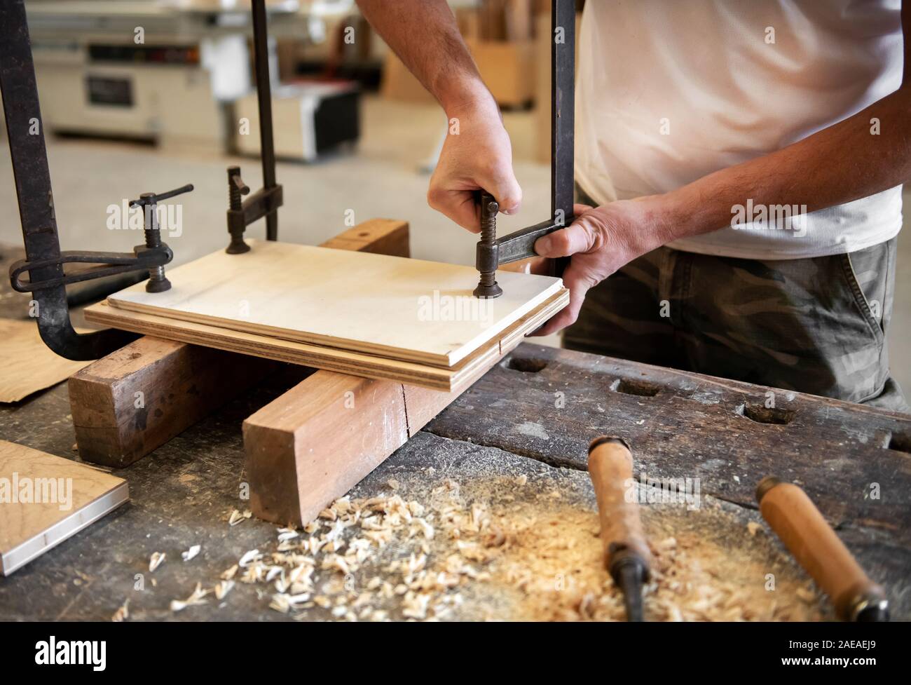 Tischler oder Schreiner mit einem Schraubstock in der Werkstatt zwei Panels von Holz zusammen Spannen manuell mit Metallklammern in Nahaufnahme auf seinem Beitreten Stockfoto