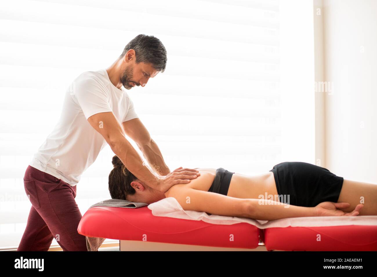 Trapezius myofasziale Behandlung in osteopath Büro Demonstration. Männlicher Arzt massiert Muskeln seiner Frau geduldig, während sie auf ihren Bauch auf Stockfoto