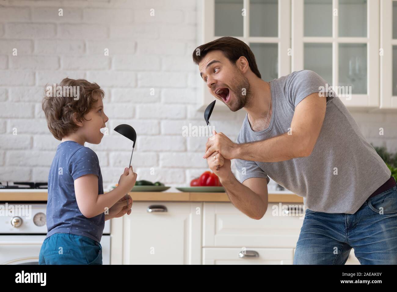 Vater tanzen mit Sohn holding Küche Löffel wie Mikrofon singen Stockfoto