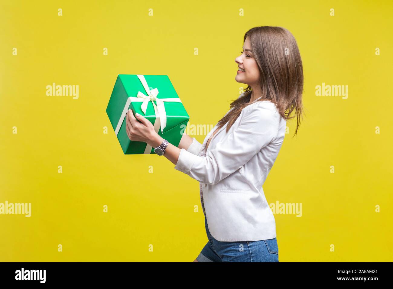 Boxing Day. Seitenansicht Portrait von charmanten großzügigen brünette Frau in Jacke und Jeans heraus halten großes Geschenk und lächelnd, glücklich zu geben. Stockfoto