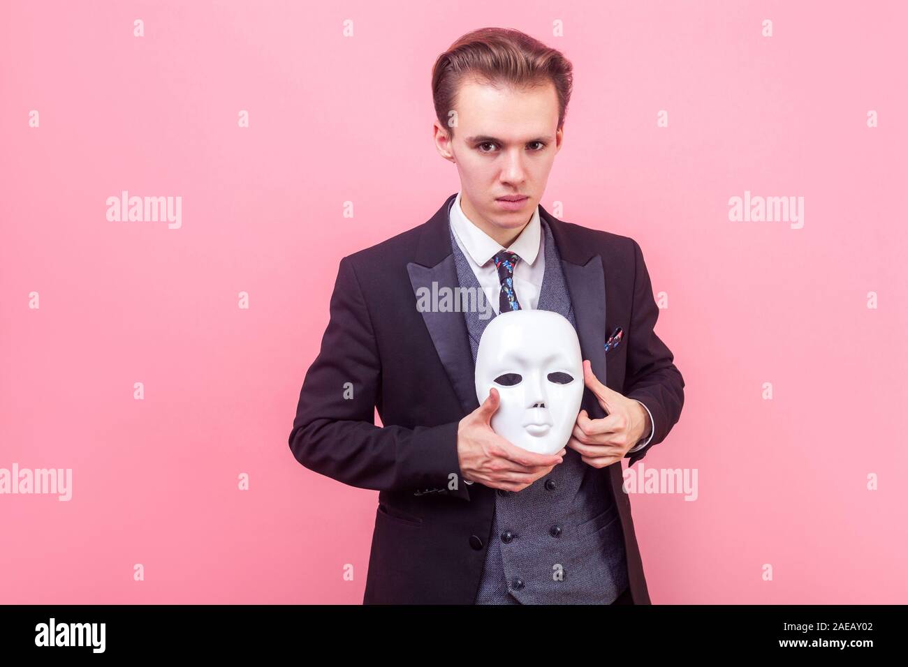 Porträt der elegante selbstbewusste Mann in Anzug mit modischen Haarschnitt Holding weisse Maske, Kamera mit konzentrierter ernstes Gesicht suchen, mehrere Pro Stockfoto