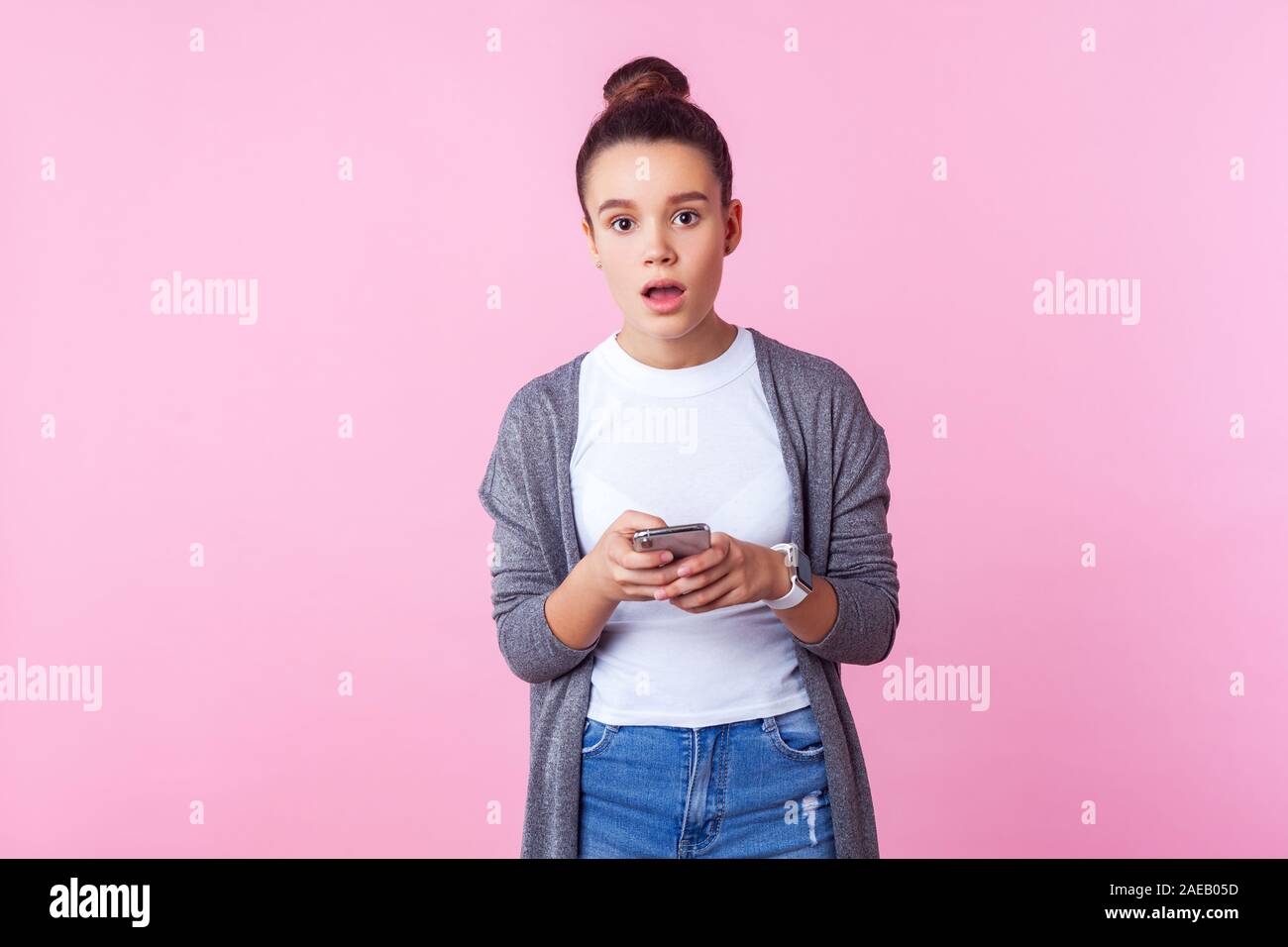 Wow, tolles Gerät! Portrait von brunette teen Mädchen mit bun Frisur in Freizeitkleidung mit Smart Phone und Kamera mit schockiert Astonish Stockfoto