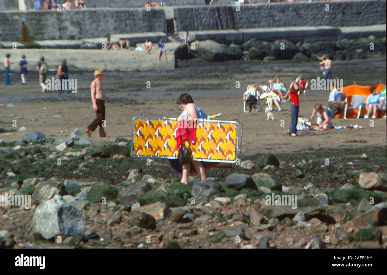 Frau mit Liegestuhl, am Strand von Robin Hoods Bay, Yorkshire East Coast, Nordengland, Großbritannien, 1973 Stockfoto