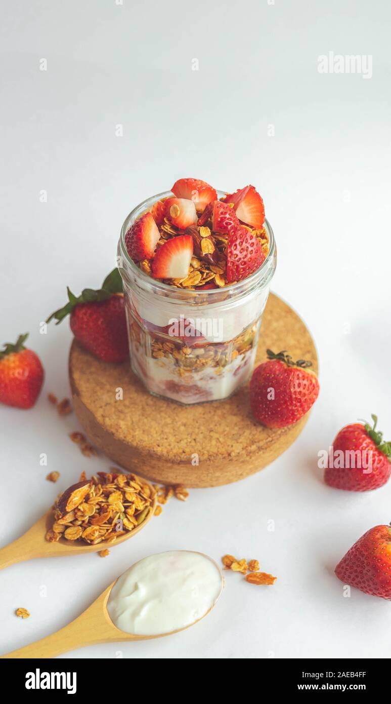 Ein Glas mit leckeren Parfaits aus gesundes Müsli, Erdbeeren und griechischer Joghurt auf weißem Hintergrund. Schuß im Winkel. Stockfoto