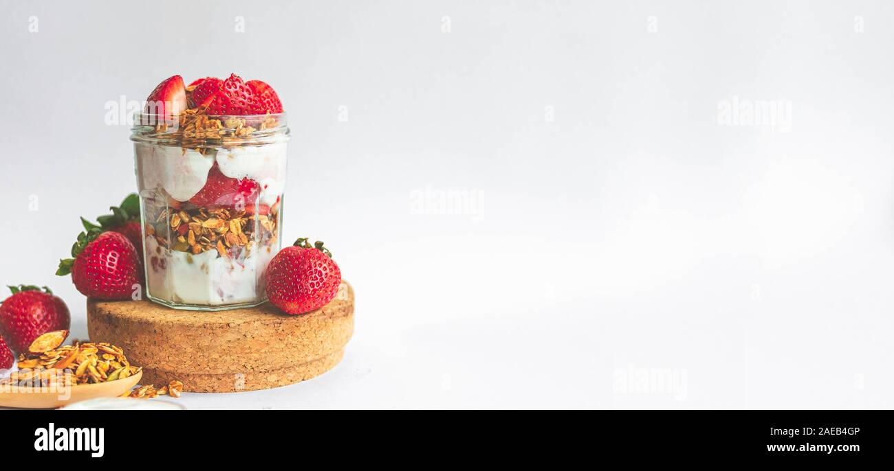 Ein Glas mit leckeren Parfaits aus gesundes Müsli, Erdbeeren und griechischer Joghurt auf weißem Hintergrund. Idee für Banner, Schuß im Winkel. Stockfoto