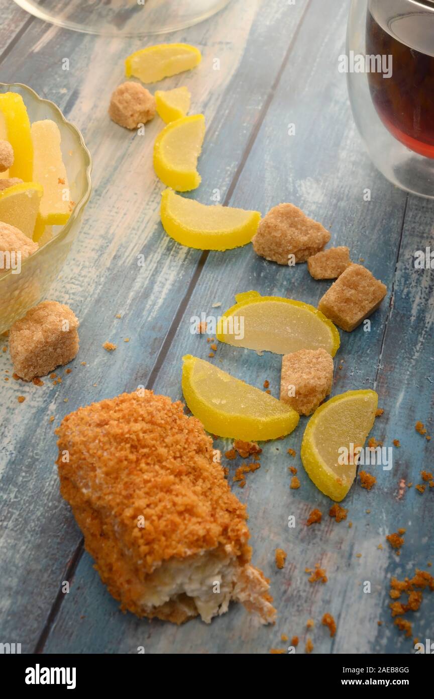 Eine gebrochene Kuchen, einem Glas schwarzen Tee, Stücke von braunem Zucker und Marmelade Zitronenscheiben auf einer hölzernen Hintergrund Stockfoto