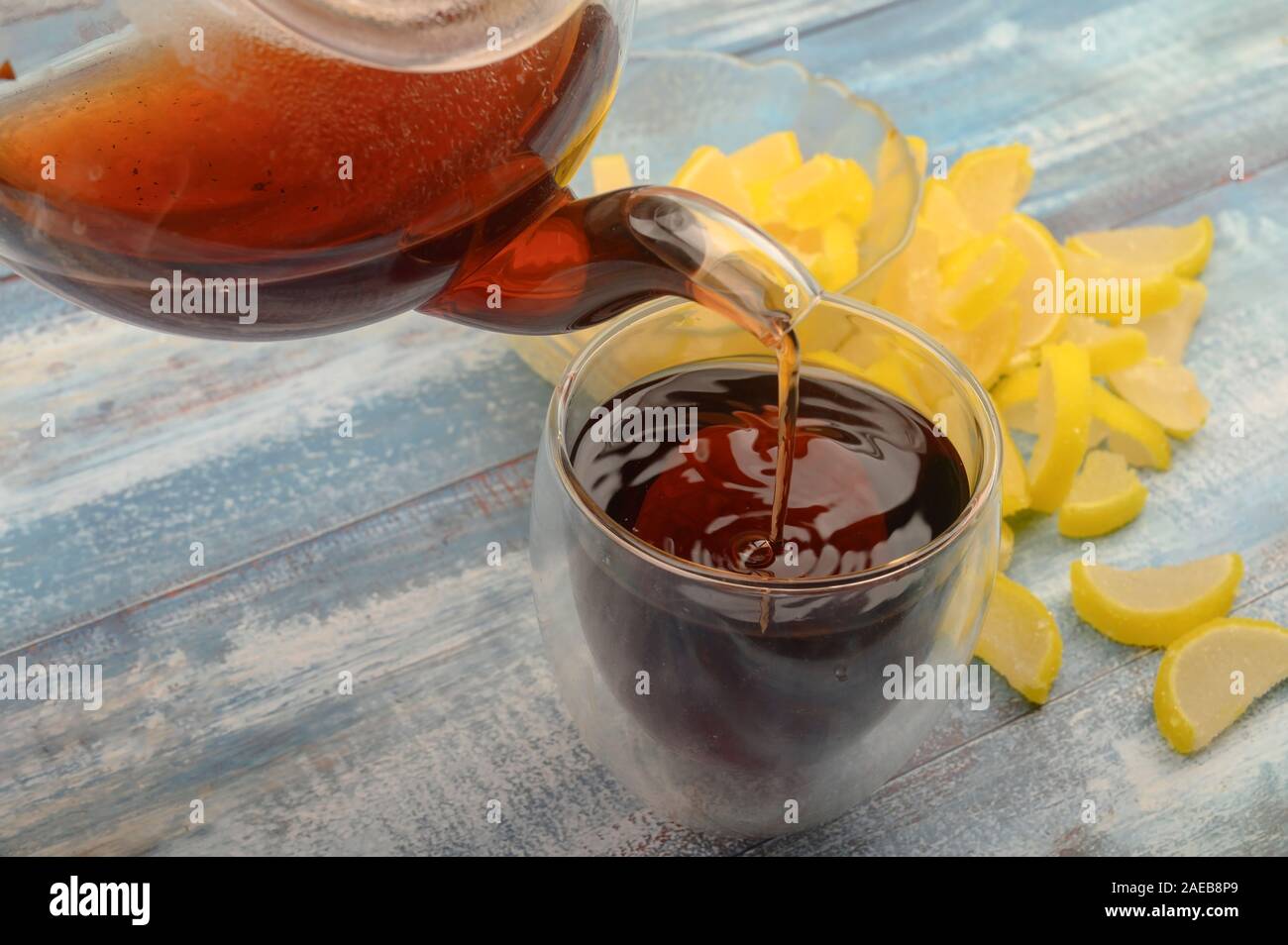 Schwarzer Tee ist aus einer Teekanne in ein Glas gegossen, Marmelade Zitronenscheiben auf einer hölzernen Hintergrund. Nahaufnahme Stockfoto