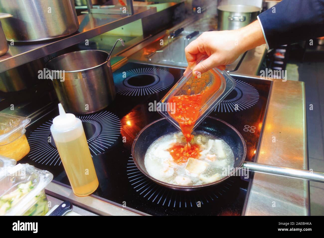 Koch ist das Hinzufügen von Tomatensauce mit Meeresfrüchten Eintopf, Arbeit in einem Restaurant Küche, getönten Bild Stockfoto
