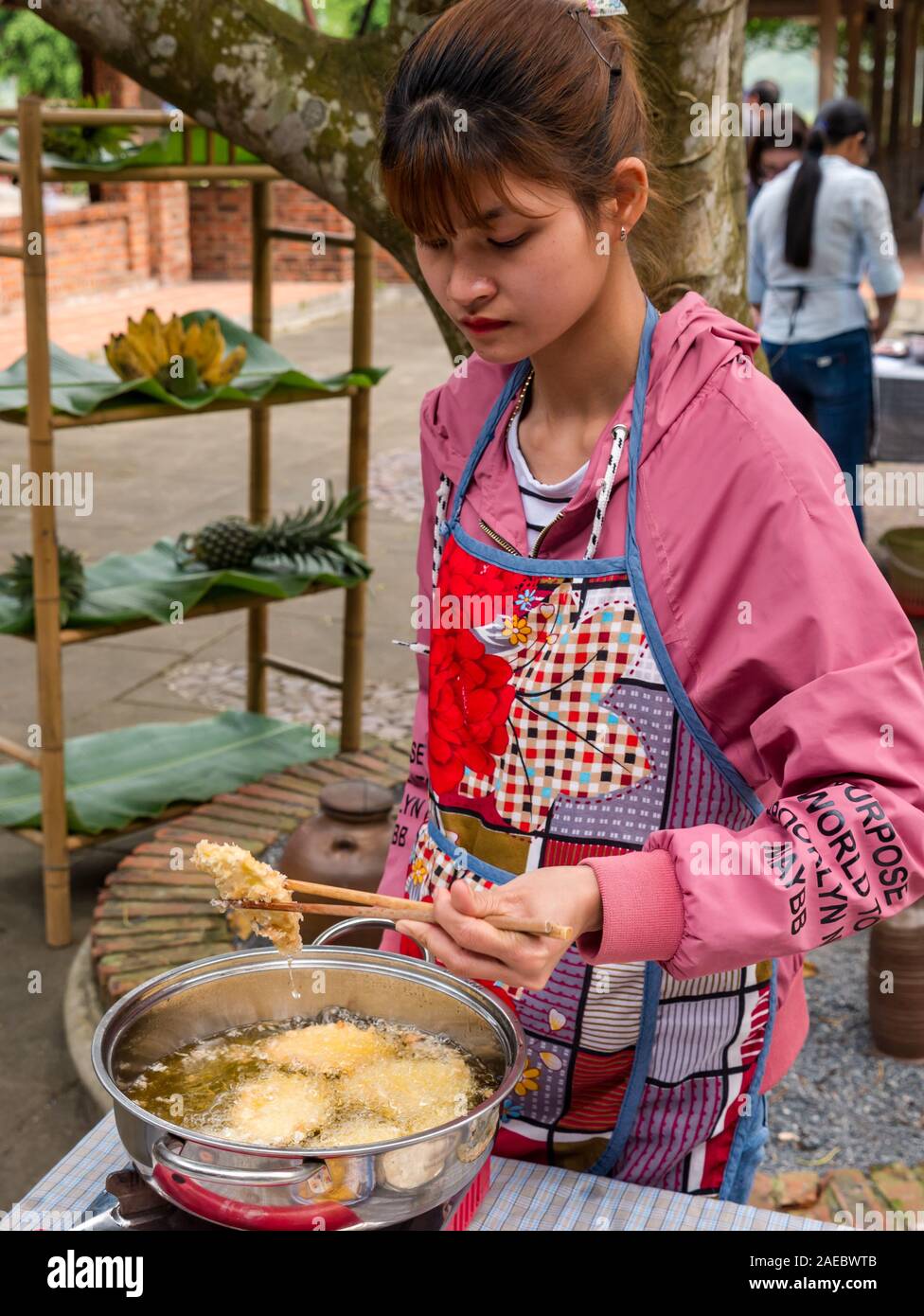 Junge Vietnamesische junge Frau kochen Frittierte süße Kartoffelpuffer mit Stäbchen an outdoor Kochkurs, Vietnam, Asien Stockfoto