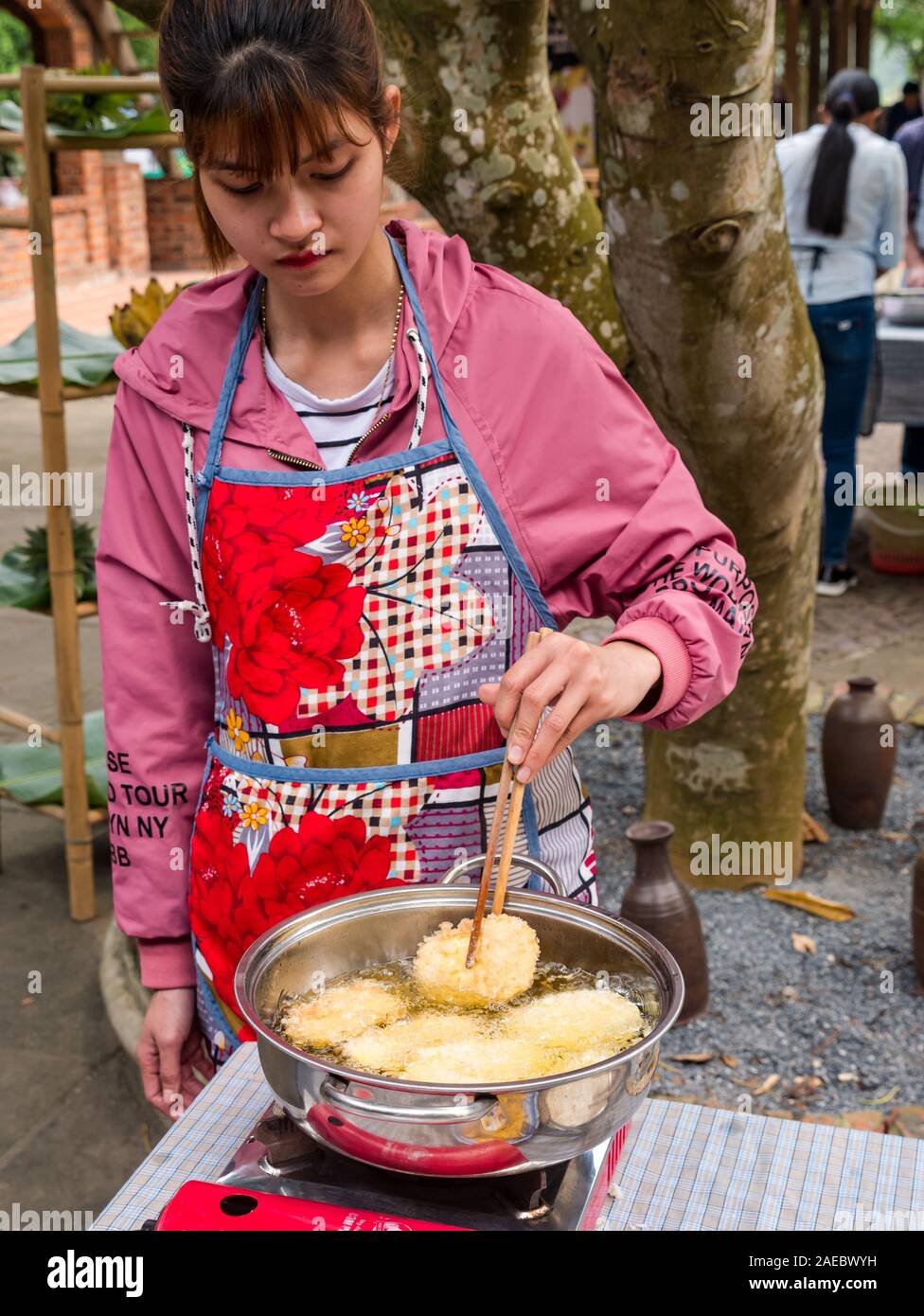 Junge Vietnamesische junge Frau kochen Frittierte süße Kartoffelpuffer mit Stäbchen an outdoor Kochkurs, Vietnam, Asien Stockfoto