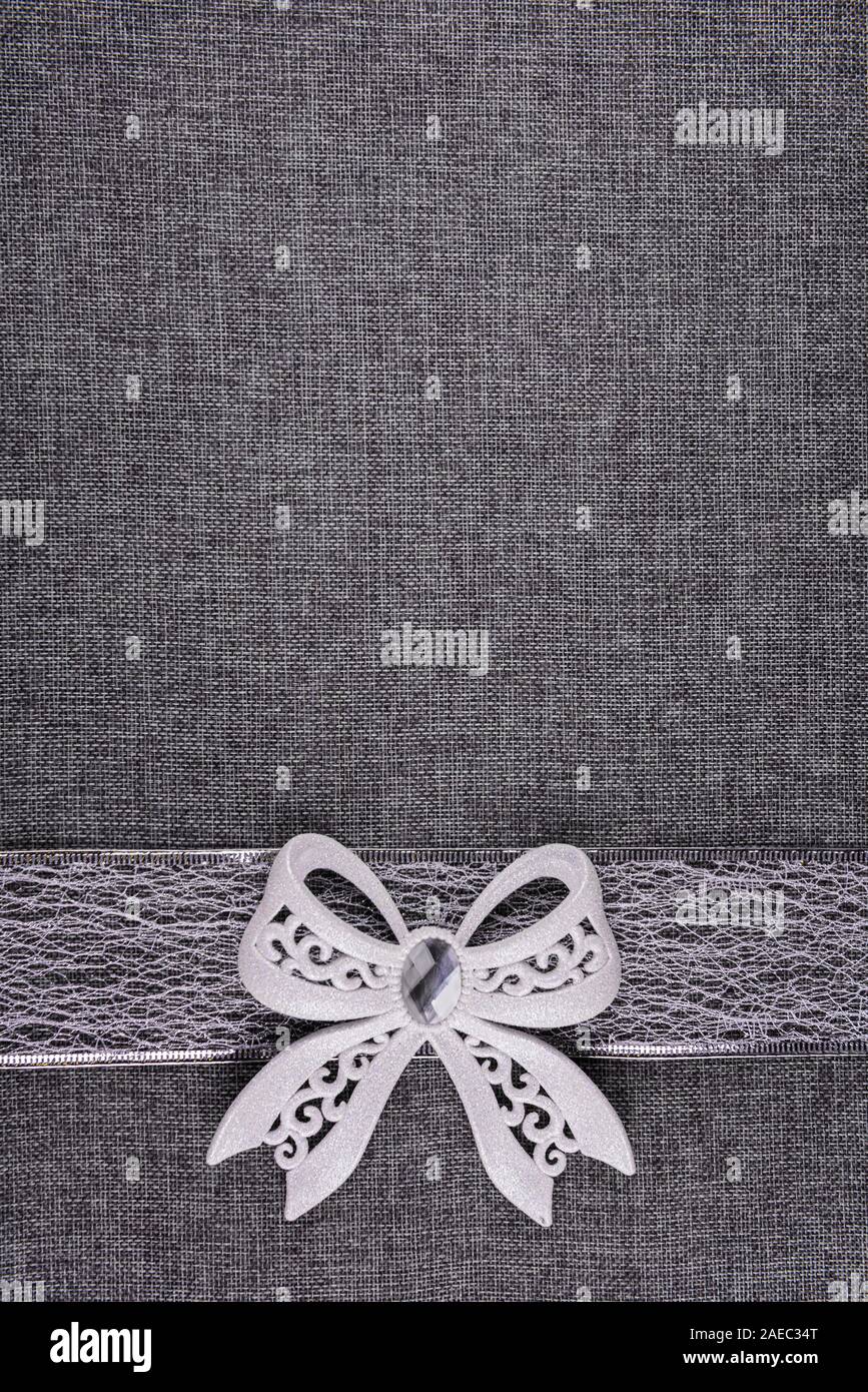 Glänzendes gebunden weiß glitter Bug auf Silber Farbband und auf Grau texturierte Sackleinen. Bogen und Band sind unten auf dem Bild. Vertic Stockfoto