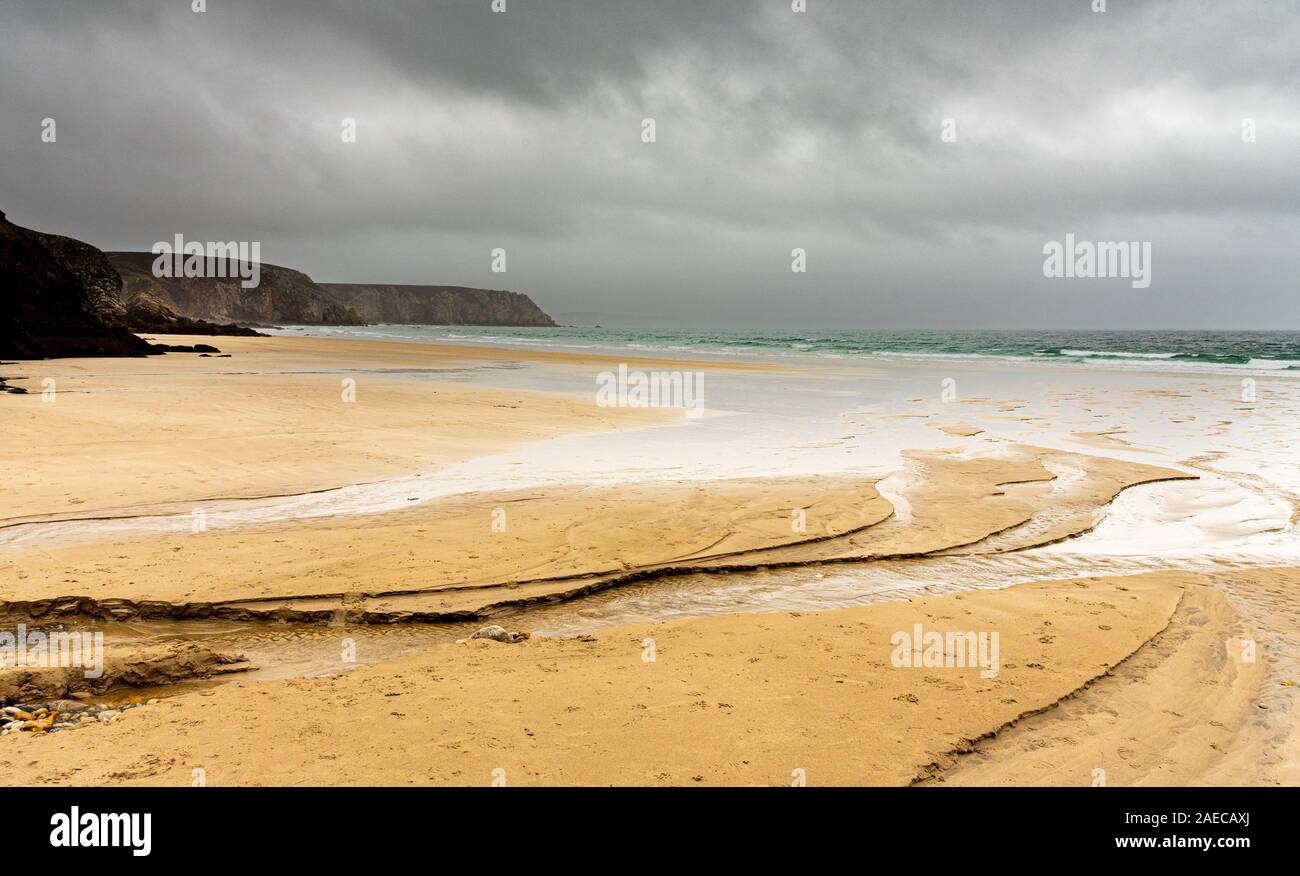 Sandstrand im Winter in der Bretagne. Wasser aus einem Fluss gräbt Kanäle, die das Meer erreichen. Die regnerischen Himmel ist in den Körpern von Wasser wider. Stockfoto