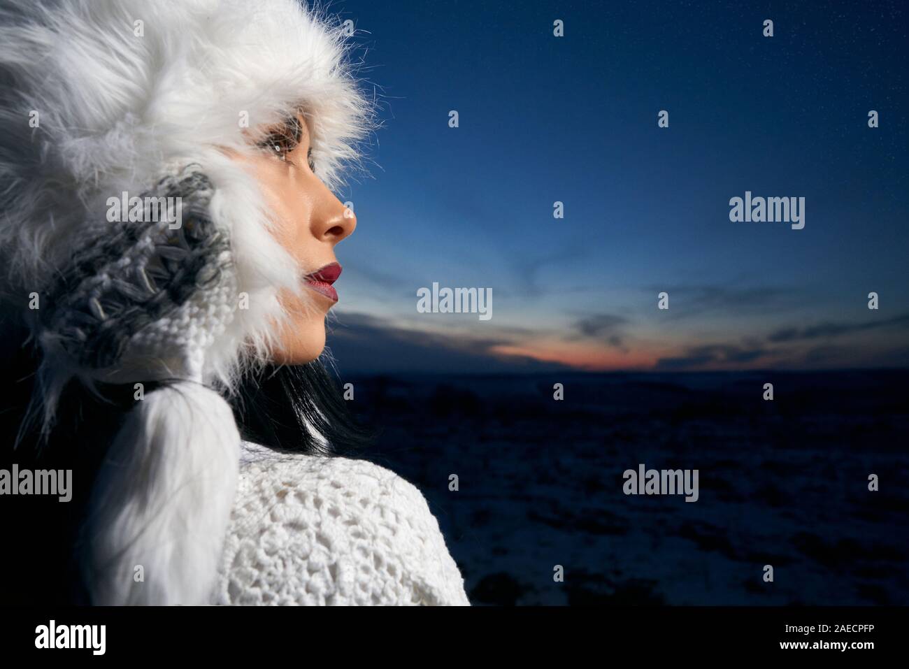 Schöne Mädchen in stilvollem Weiß gestrickte Bluse und weisse warme Mütze auf dem Hintergrund von Feld- und Abendhimmel posieren. Modell berührt hat und oben zu schauen. Konzept der Winterbekleidung. Stockfoto